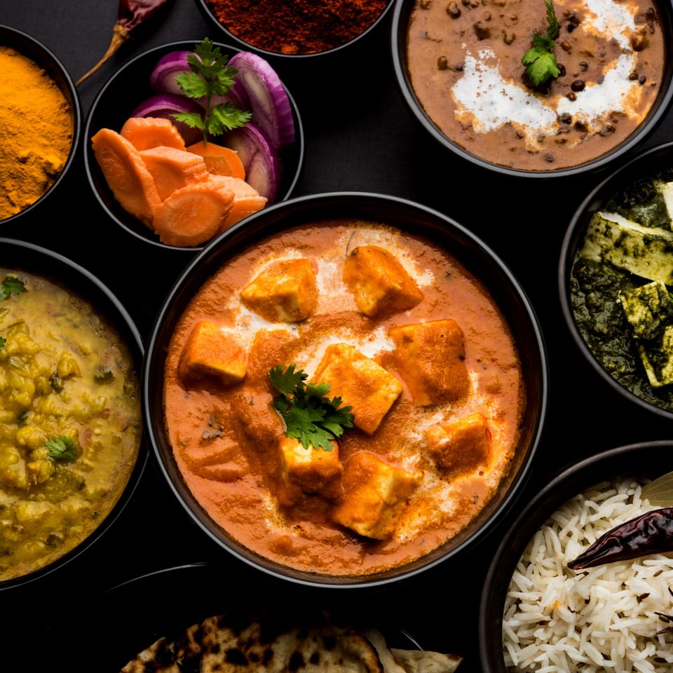 Overhead view of various Indian dishes including paneer butter masala, dal makhani, palak paneer, and rice.