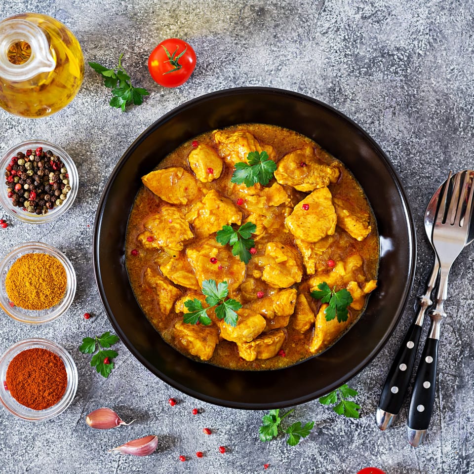 Overhead view of Everest Indian Kitchen's chicken curry with spices, oil, and tomatoes.