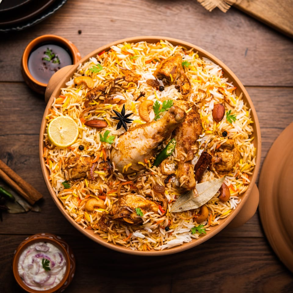 A large bowl of Everest Indian Kitchen's chicken biryani with lemon, nuts, and spices.